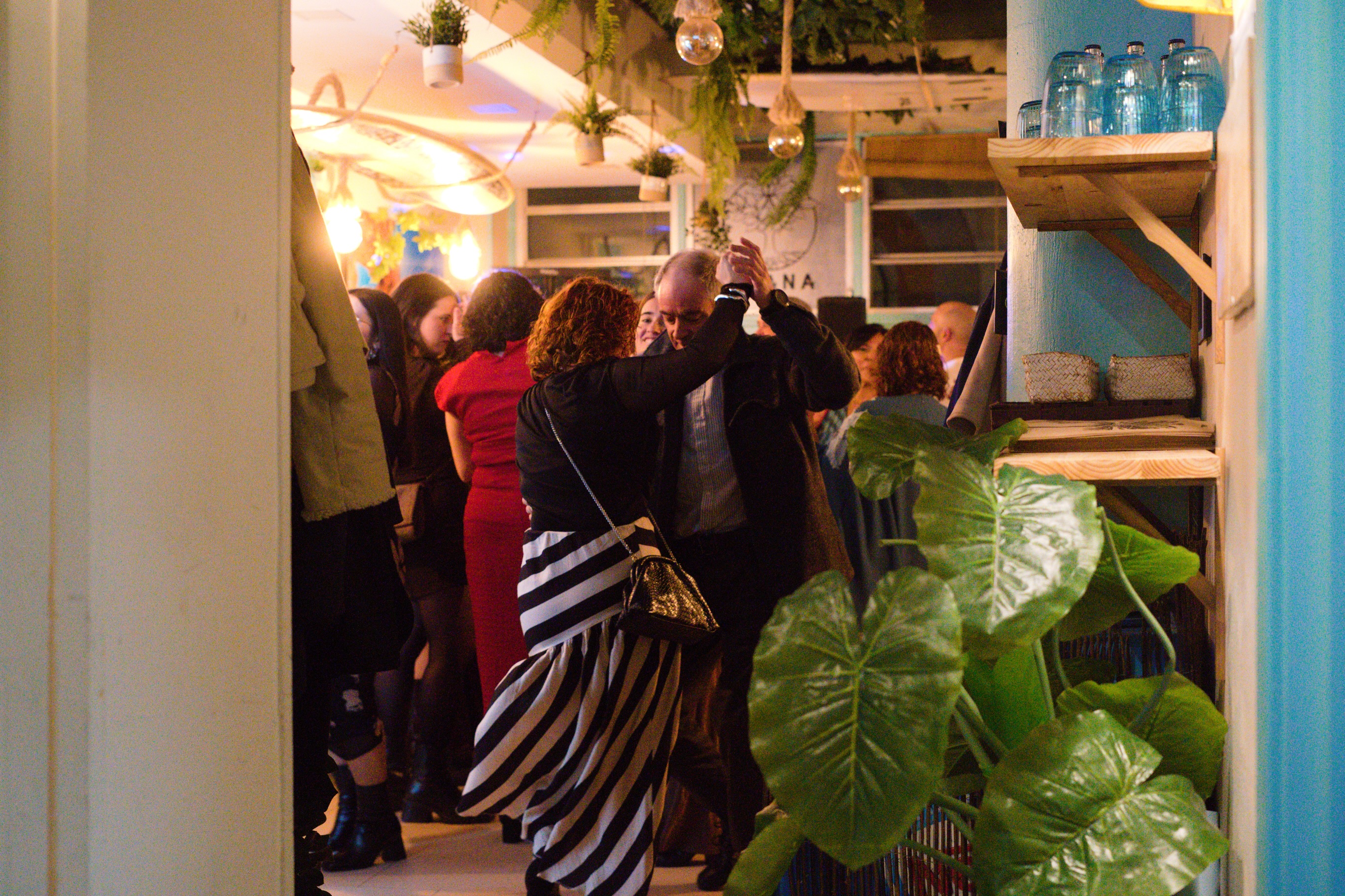 El local de Ohana de noche, lleno de gente, con plantas colgantes y una tabla de surf en el techo